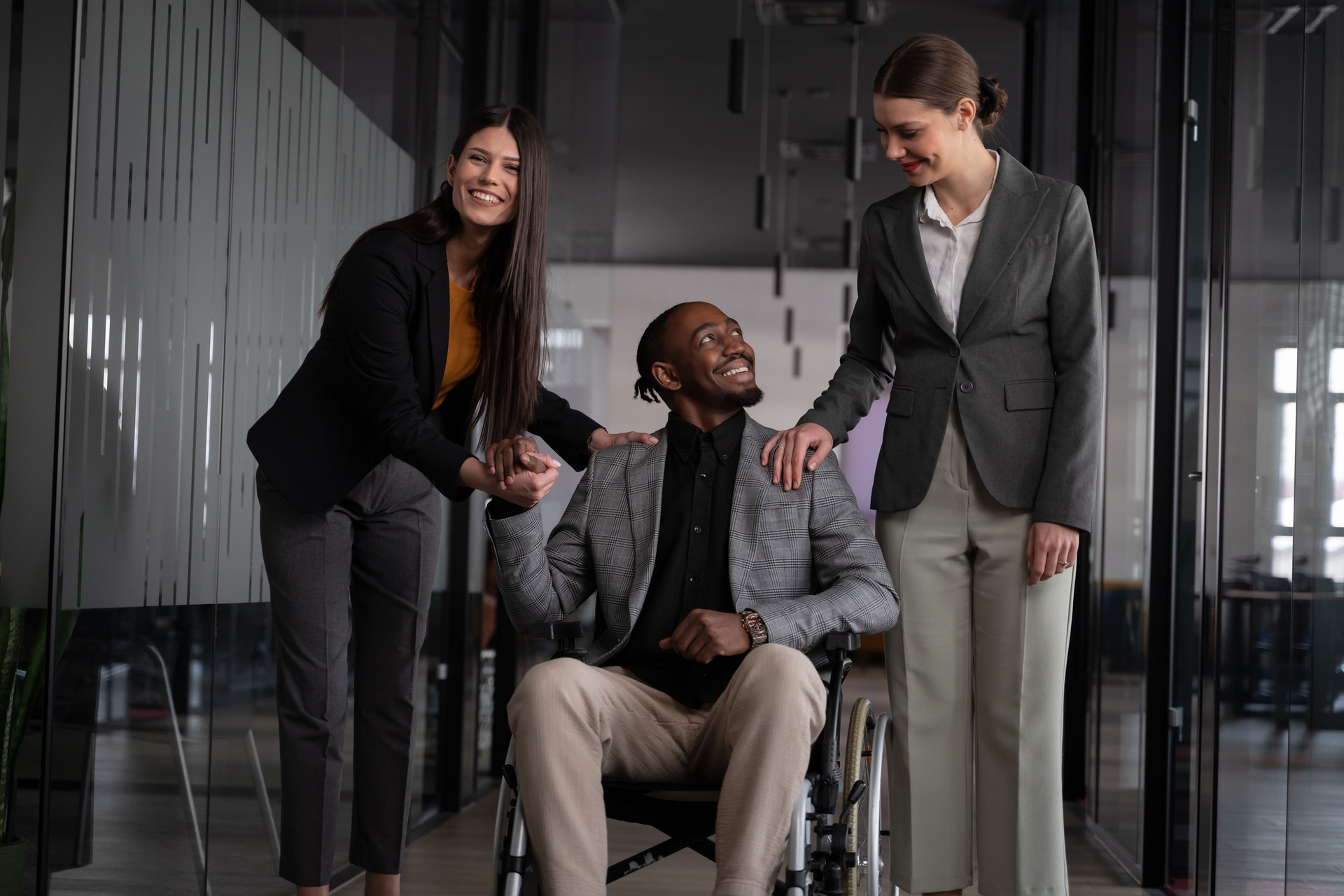 Diverse business team supporting a colleague in a wheelchair in a modern office. Concept of workplace inclusion, teamwork, and professional collaboration in corporate settings