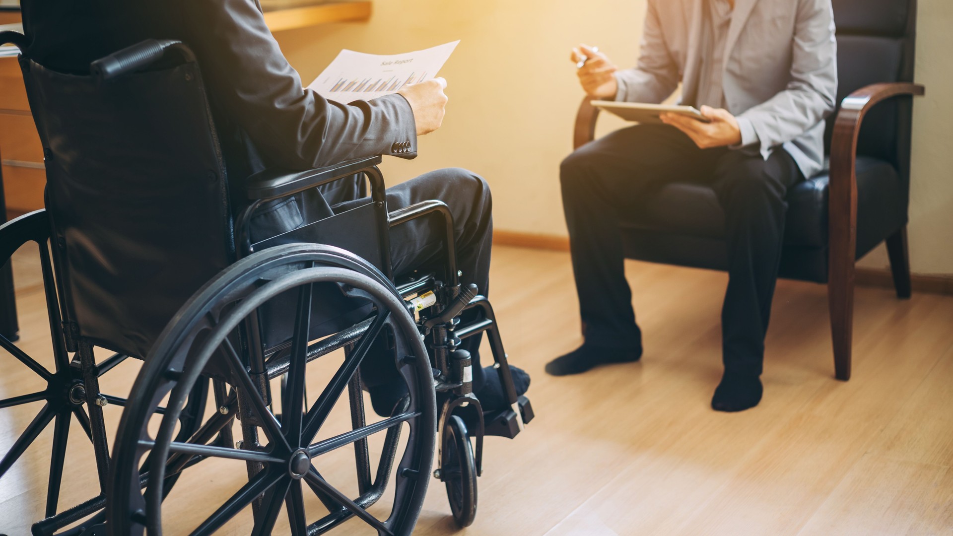 Man on wheelchair with his boss. After car accident and rehabilitation, a businessman can return to work again.