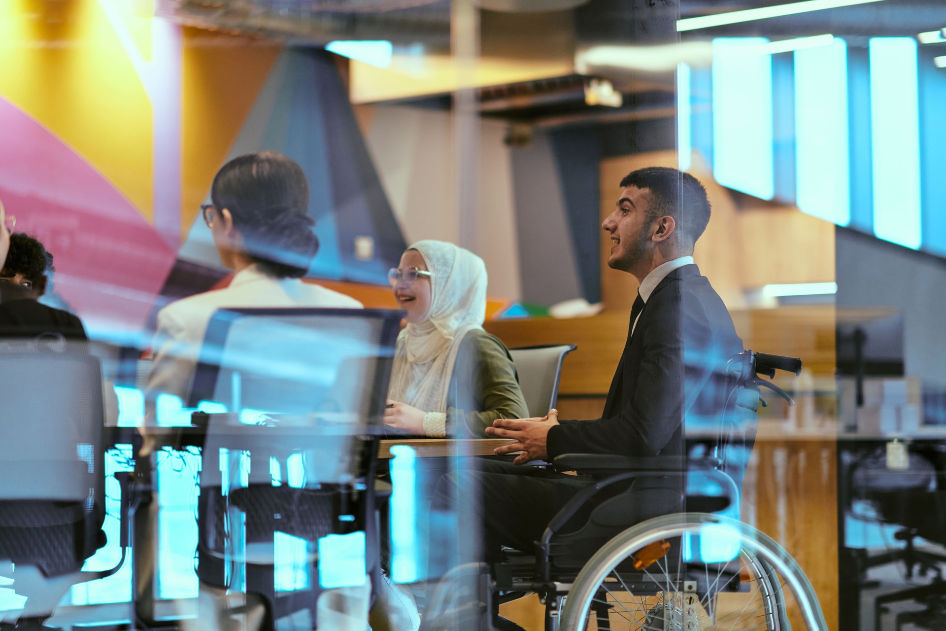 In a modern glass startup office, a wheelchair-bound director leads a successful meeting with colleagues, embodying inclusivity and teamwork.