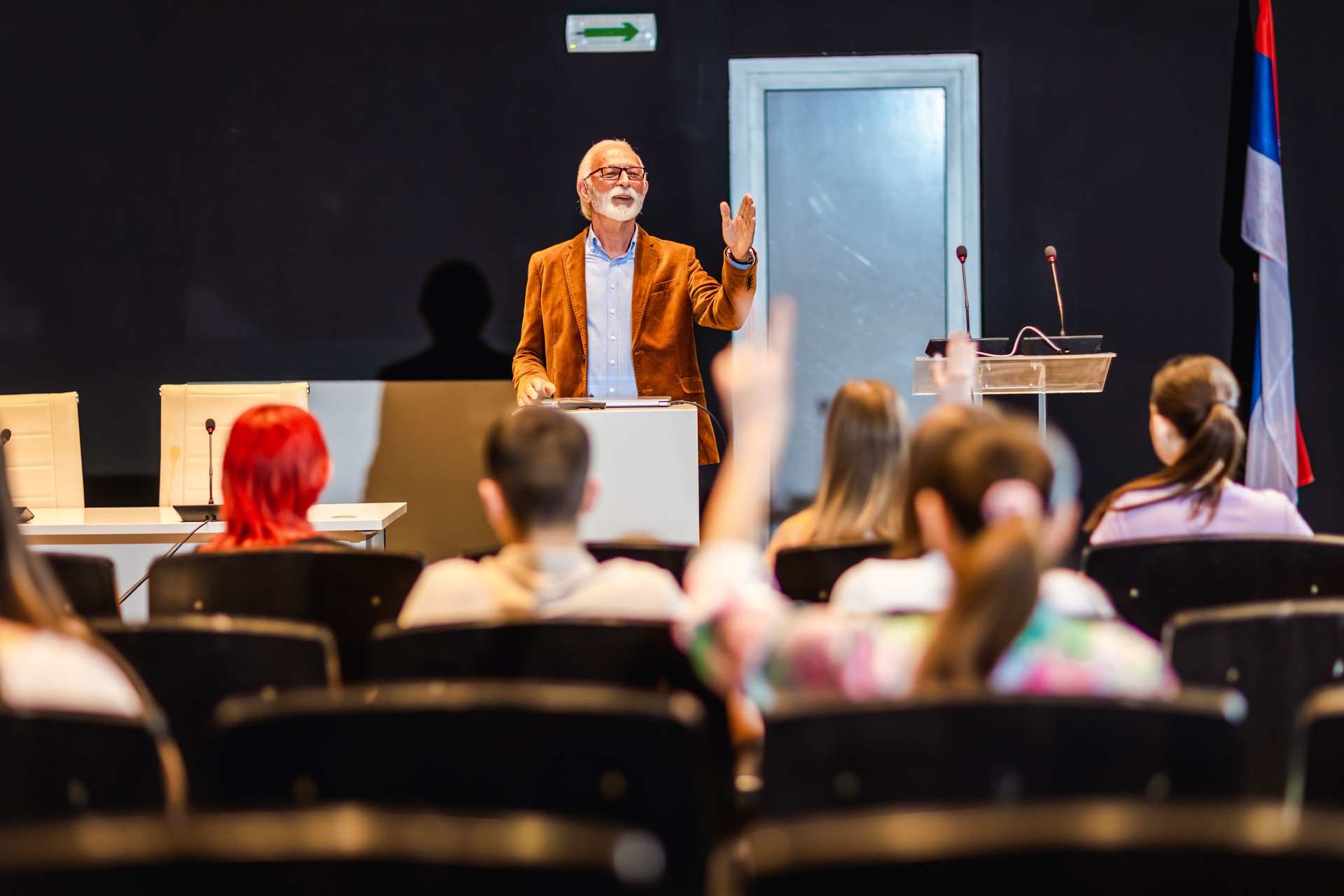 Male elderly professor lecturing students in amphitheater. Choosing which student is going to give him an answer.
